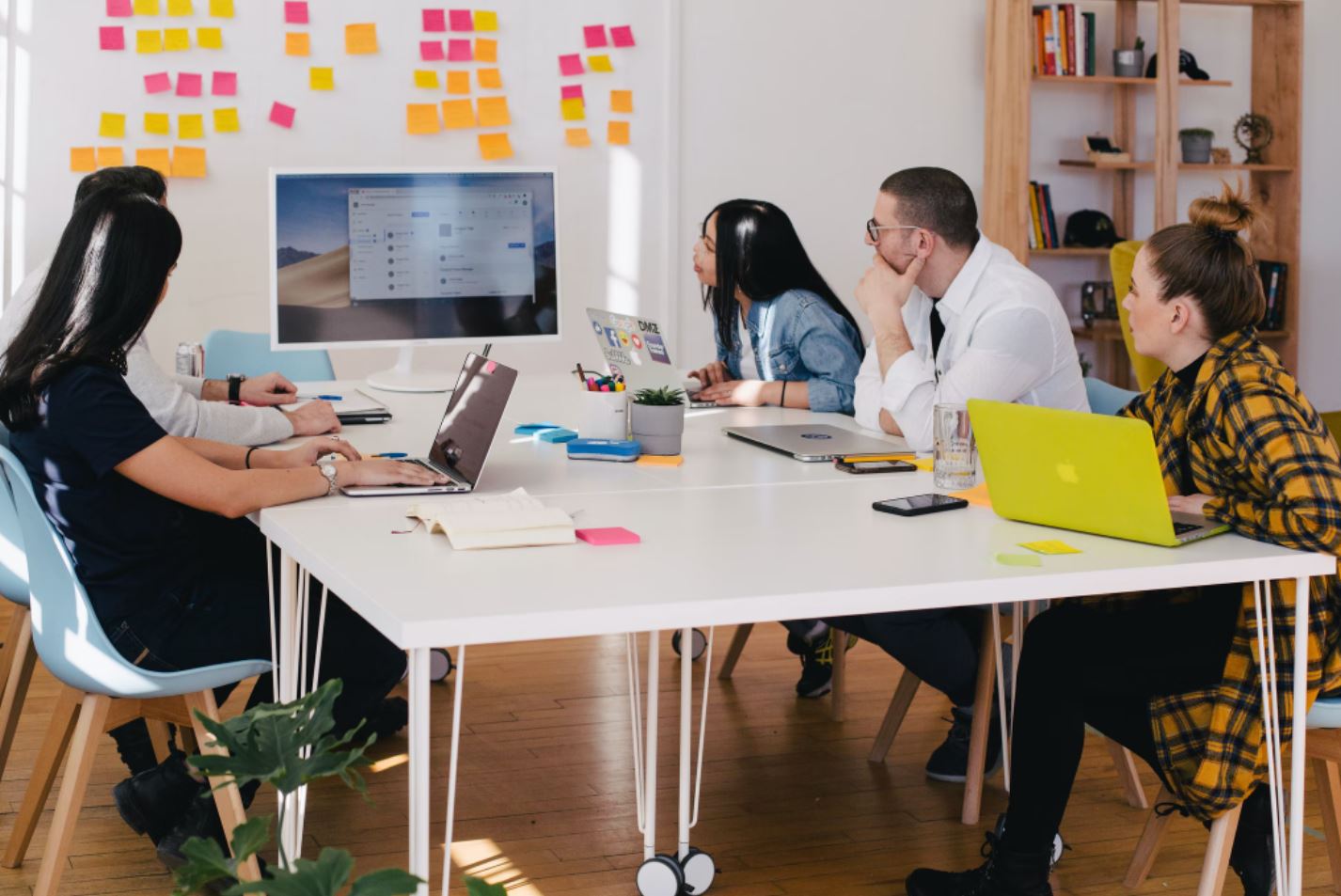 A group of five people sitting around a table in a meeting looking at a computer screen