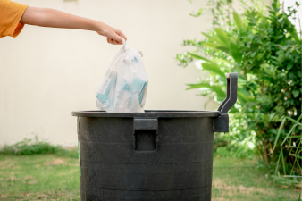 A hand placing trash into a garbage bin
