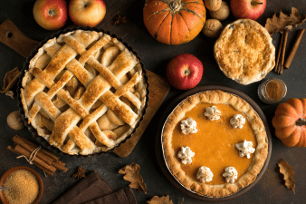 Large apple and pumpkin pies on a brown surface surrounded by apples, pumpkins, and other fall items